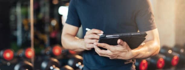 Hands taking notes on a tablet beside the dumbbell rack